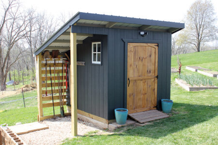 dark blue shed with overhand to store tools and a brown door